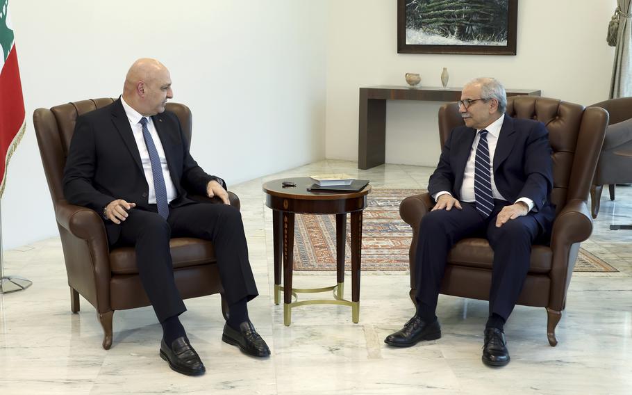 Two men in suits sit in sofa chairs and look at one another.
