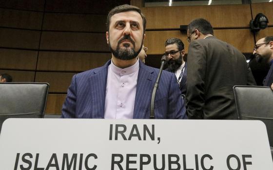 An Iranian man in a suit sits at a microphone behind a placard on the table denoting his country.