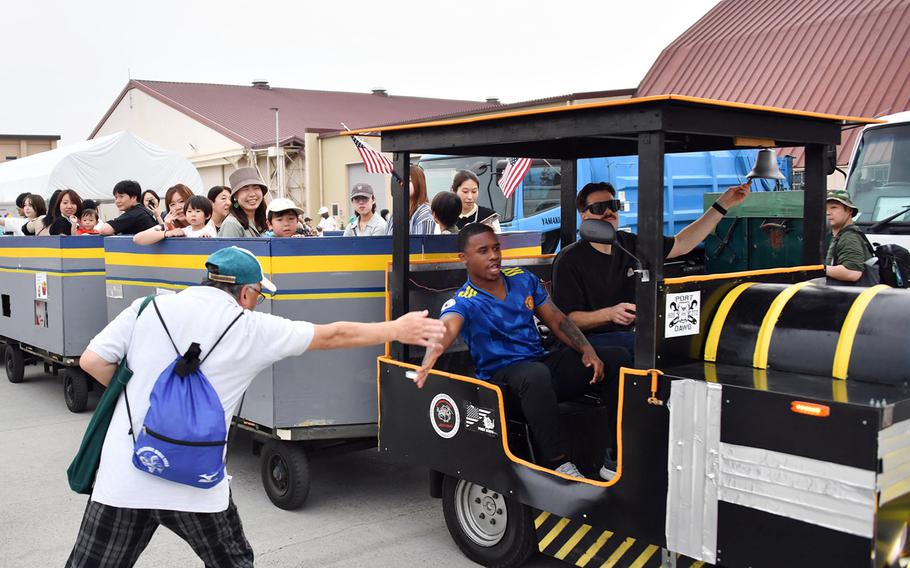 A Japanese man with a backpack reaches out to high-five an airman sitting on the passenger side of the first car of a tourist train filled with visitors.