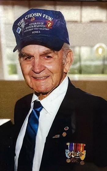 A vertical photo of a man wearing a blue hat that reads “The Chosin Few” with military pins on his lapel.