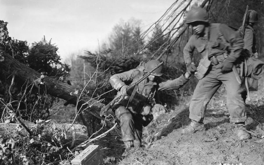 Army Pfc. Benny Barrow of St. Louis, Missouri, gives a helping hand to a buddy as they make a difficult climb in the Hurtgen Forest in Germany during World War II. 