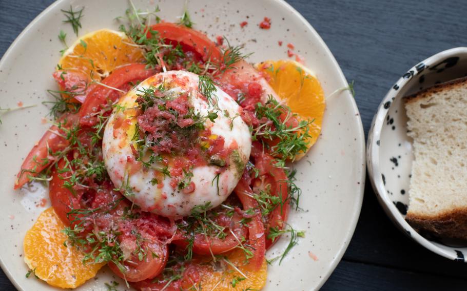 A ball of burrata sits on a bed of tomato and orange slices.