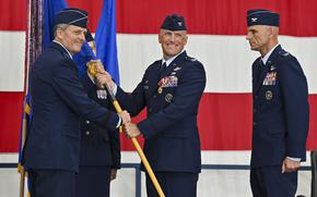 Several senior airmen in uniform, two of whom are exchanging a banner.