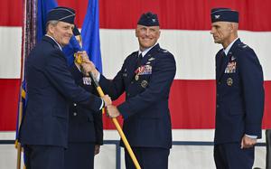 Several senior airmen in uniform, two of whom are exchanging a banner.