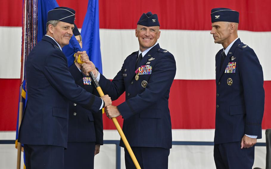 Several senior airmen in uniform, two of whom are exchanging a banner.