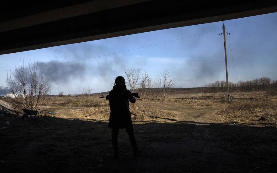A Ukrainian forces under a damaged bridge on Irpin as smoke is seen over the city of Bucha where Russian forces are fighting against Ukrainian forces on March 12, 2022.