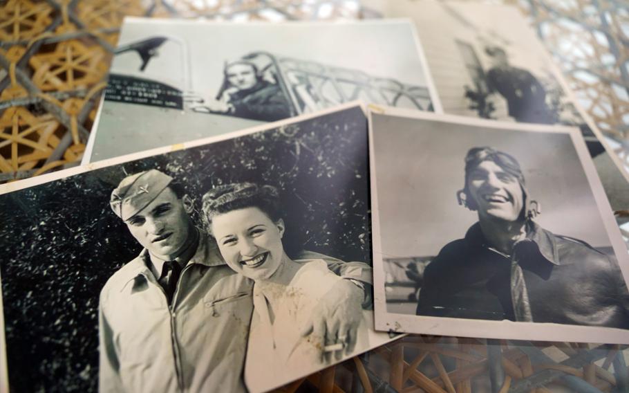 Black-and-white, 1940s-era photographs lie on a table depicting an aviator in a leather jacket and helmet and a man in a military dress uniform posing with his arm around a smiling woman in white.