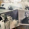 Black-and-white, 1940s-era photographs lie on a table depicting an aviator in a leather jacket and helmet and a man in a military dress uniform posing with his arm around a smiling woman in white.