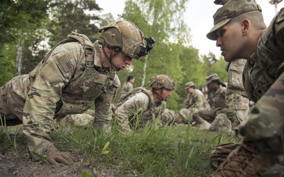 Several soldiers do pushups as others crouch and watch them.