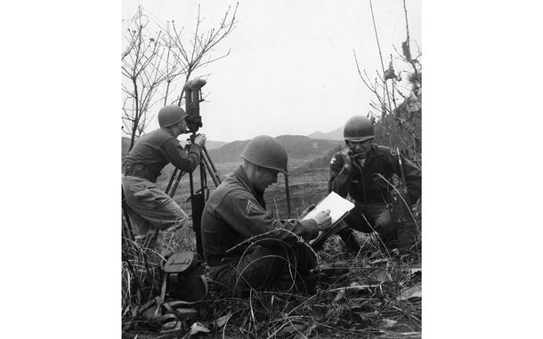 A black and white photo of soldiers doing various things: one looking into a device, another on the phone and a third writing something down.