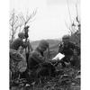 A black and white photo of soldiers doing various things: one looking into a device, another on the phone and a third writing something down.