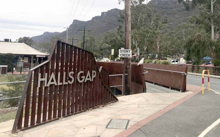 A metal slatted sign next to a road says Halls Gap.