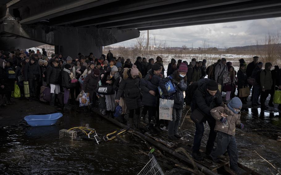 Ukrainians crowd under a destroyed bridge as they try to flee crossing the Irpin river in the outskirts of Kyiv, Ukraine, Tuesday, March 8, 2022. 