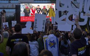 People hold up signs as they gather in front of a TV screen that shows a hostage being released from captivity by masked militants.