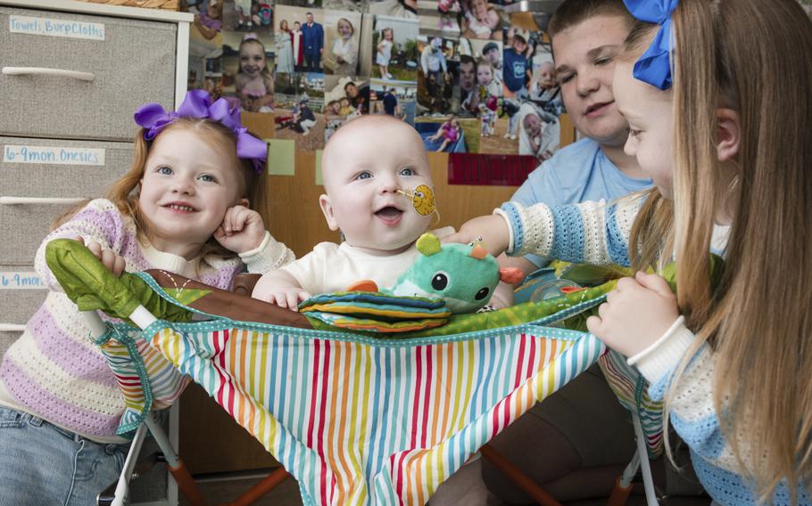 A baby between other children smiles.