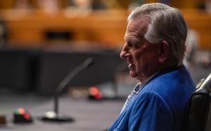 Tommy Tuberville, wearing a blue suit and seen from the side, sits at a table in a congressional hearing room.