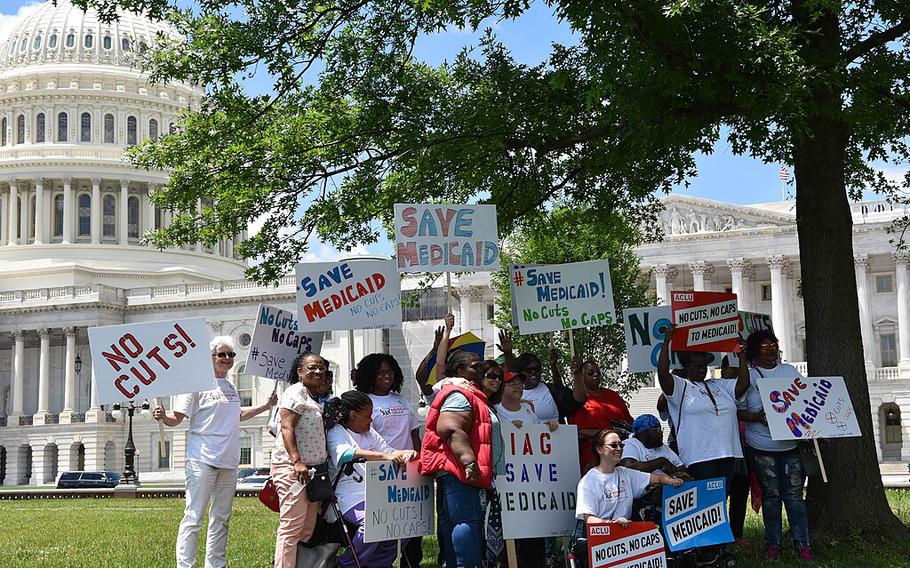 Protesters stand under a tree holding signs in front of the U.S. Capitol.