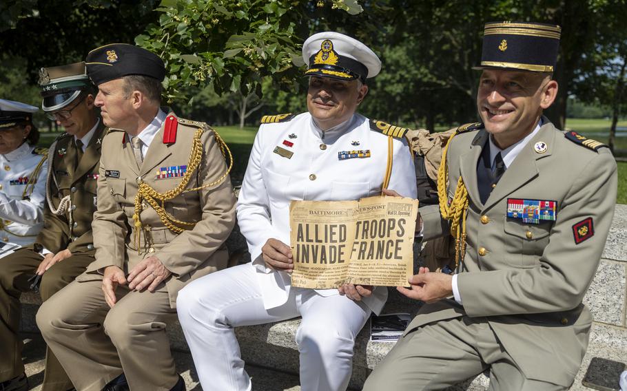 Men in formal military attire hold an old newspaper page with the headline “ALLIED TROOPS INVADE FRANCE.”