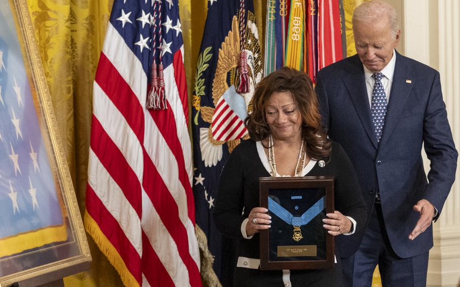 An elderly woman holds a framed Medal of Honor awarded posthumously to her father while standing next to Joe Biden.