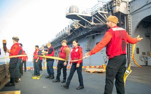 Sailors holding a line walk across the deck of a ship.