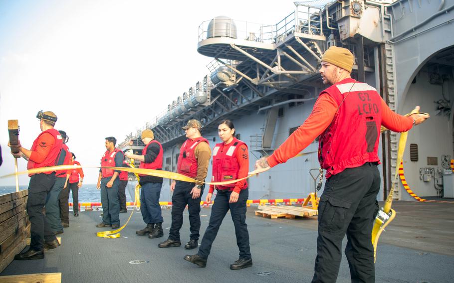 Sailors holding a line walk across the deck of a ship.