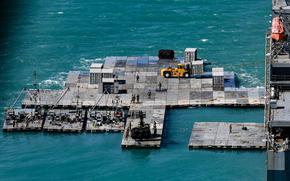 Army mariners work to construct a causeway adjacent to the MV Maj. Bernard F. Fisher off the coast of Bowen, Australia, July 28, 2023. When complete, the causeway will form a floating pier enabling the discharge of vehicles from the Fisher to shore demonstrating the critical capability of Joint Logistics Over-the-Shore (JLOTS) during Talisman Sabre. JLOTS demonstrates the critical capability of bringing vehicles and equipment to the shore in austere environments or when port facilities are unavailable. Talisman Sabre is the largest bilateral military exercise between Australia and the United States, with multinational participation, advancing a free and open Indo-Pacific by strengthening relationships and interoperability among key allies. (U.S. Army photo by Sgt. David Resnick)