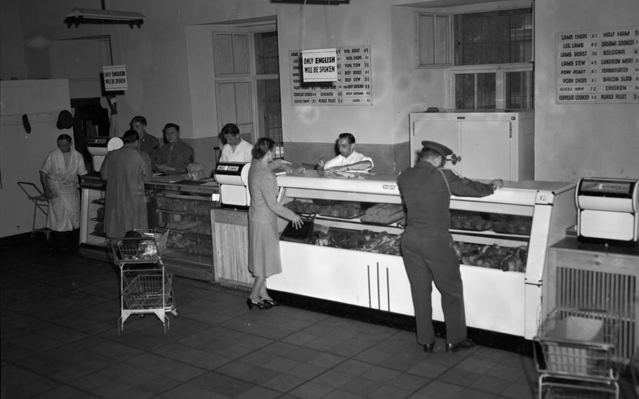 A black and white photo of people lined up at the butcher counter of a store.