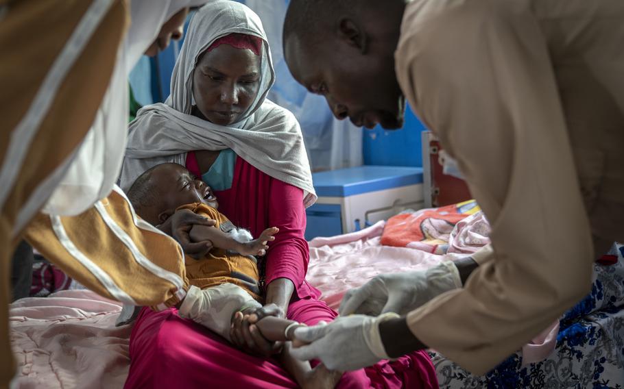 Scheharazad Muhamed Ahmed, 25, holds her 15-month-old son, Eyaad Ahamday, as nurses administer a treatment at the Doctors Without Borders pediatric malnutrition ward at El Geneina Teaching Hospital. Eyaad, a sole surviving triplet who was born prematurely, suffers from anemia because Scheharazad, who is malnourished, cannot produce enough breastmilk to feed him.