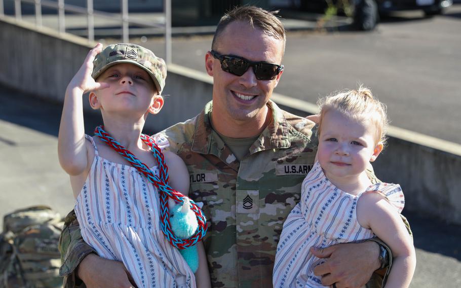 A soldier wearing sunglasses holds two kids in his arms.