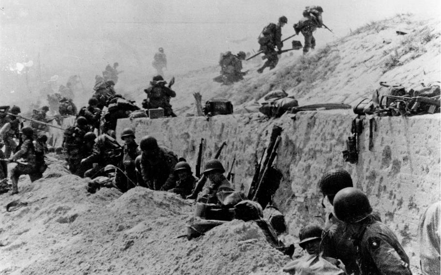 U.S. Soldiers of the 8th Infantry Regiment, 4th Infantry Division, move out over the seawall on Utah Beach, after coming ashore. Other troops are resting behind the concrete wall. Photo dated 9 June 1944, but probably taken on D-Day, 6 June 1944.  