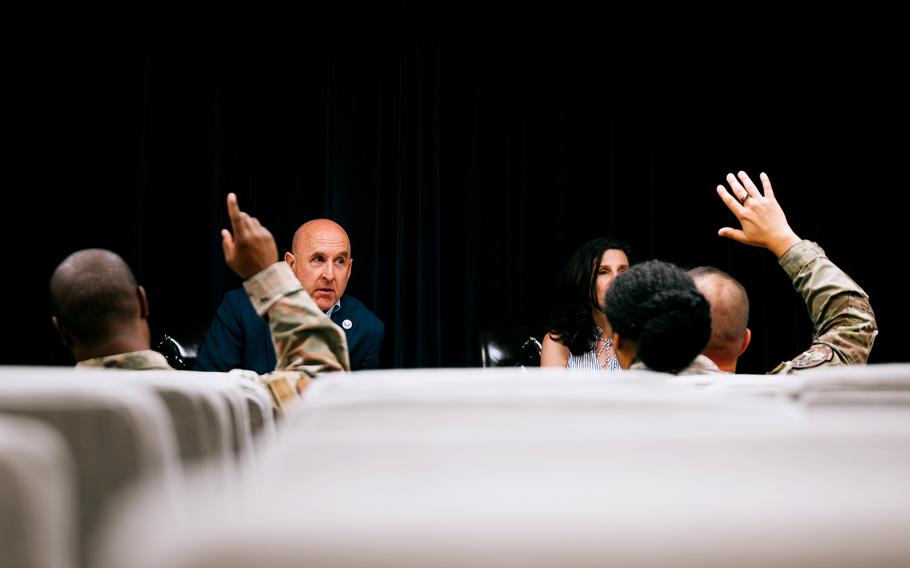 Several people are seen raising their hands from a distance, mostly obscured by out-of-focus seats in the foreground.
