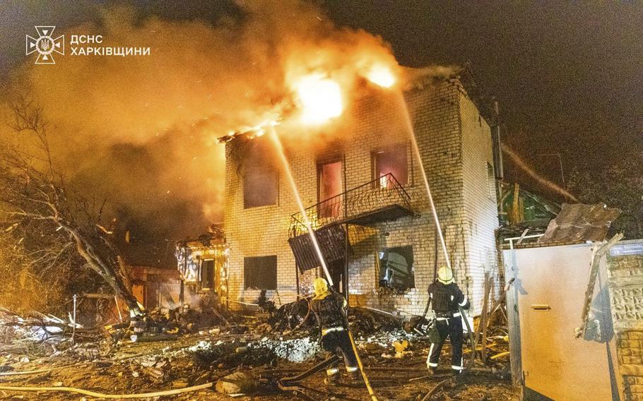 Firefighters spray hoses at the top of a two-story building on fire.