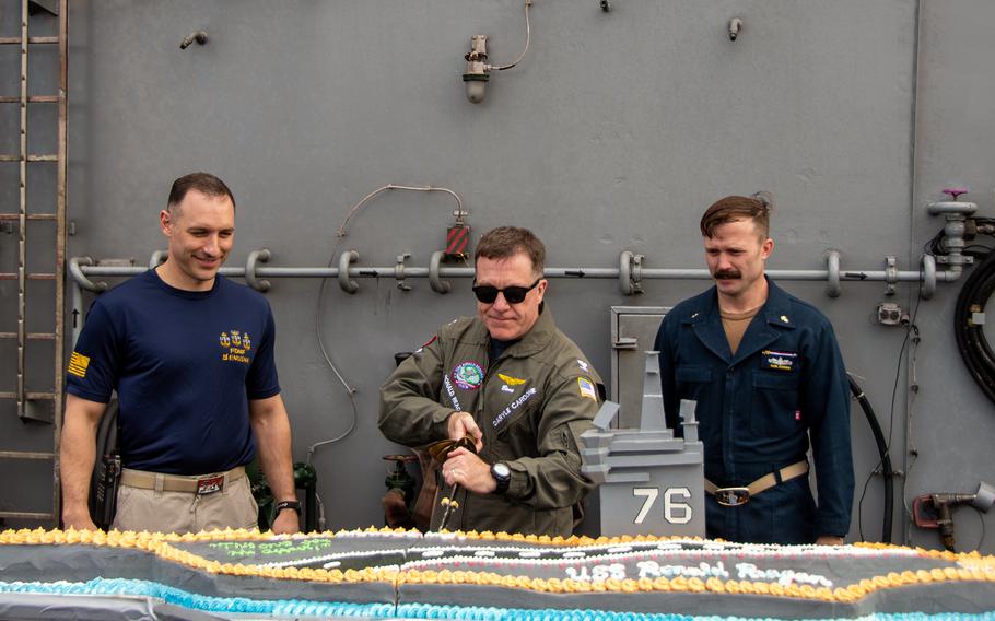 The USS Ronald Reagan's skipper, Capt. Daryle Cardone, slices into a cake shaped like the aircraft carrier during a 20th anniversary celebration somewhere in the Indian Ocean, July 30, 2023. 