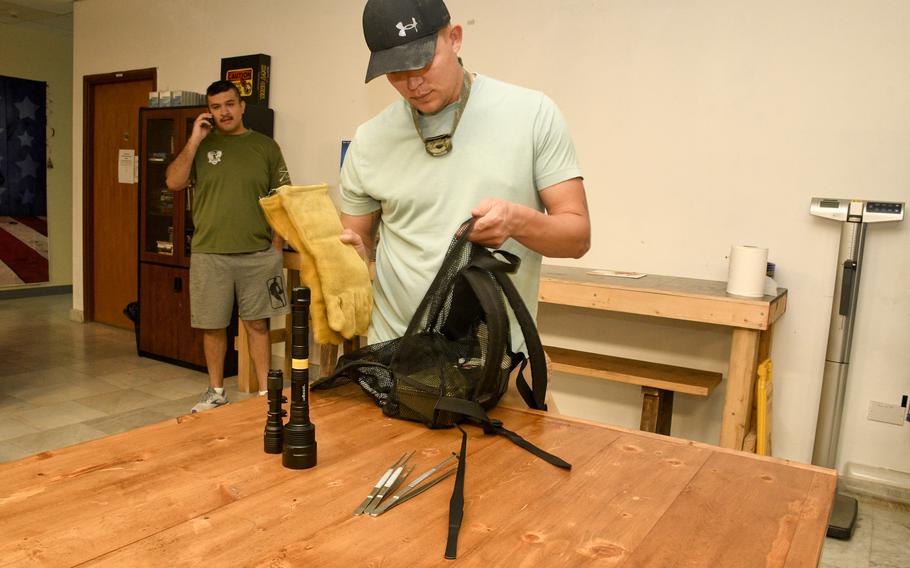 Army Spc. Joseph Neitz, right, packs up protective gloves, metal tongs and ultraviolet flashlights into a bag he uses for scorpion hunting. Neitz and Air Force Staff Sgt. Adan Guzman, left, lead troops and contractors on trips into the desert night to collect scorpions and camel spiders.