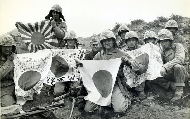 Ten Marines pose with Japanese “good luck” flags in a black and white picture from 1945.