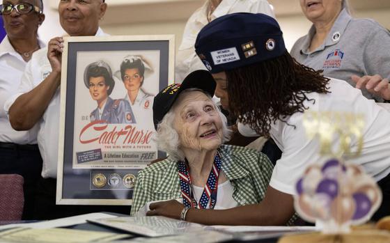 A member of the Women Veterans of Nevada hugs a seated centinarian wearing a World War II veteran hat.