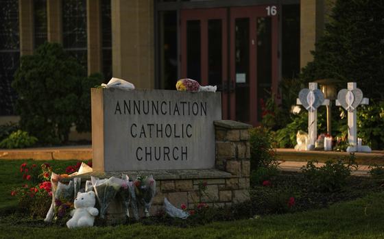 A sign that reads “Annunciation Catholic Church” with numerous bouqets and a stuffed animal placed around it.