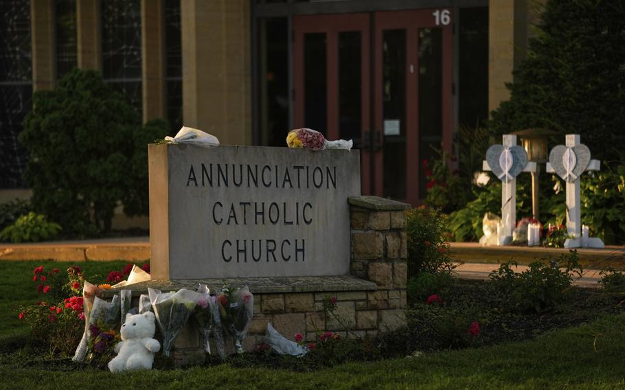 A sign that reads “Annunciation Catholic Church” with numerous bouqets and a stuffed animal placed around it.