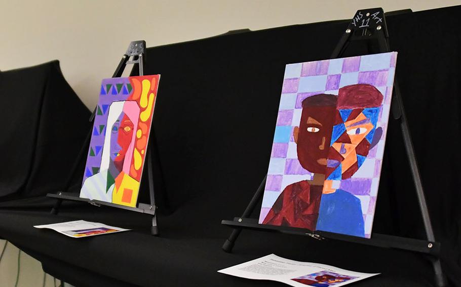 Two colorful self portraits sit on display against a black backdrop on a table. 