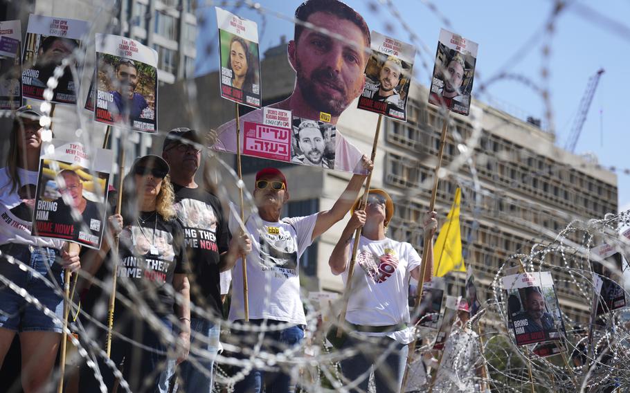 People carry signs, some with faces of hostages on them, as they stand behind barbed wire.