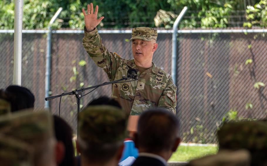 Brig. Gen. James Dooghan raises a hand while standing at a podium in uniform to speak.