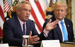 An in-focus HHS Secretary Robert F. Kennedy Jr. speaks as an out-of-focus President Donald Trump watches next to him.