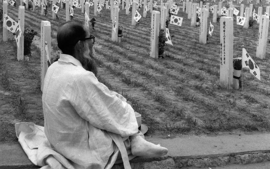 An old man contemplates the rows of white markers for the dead.