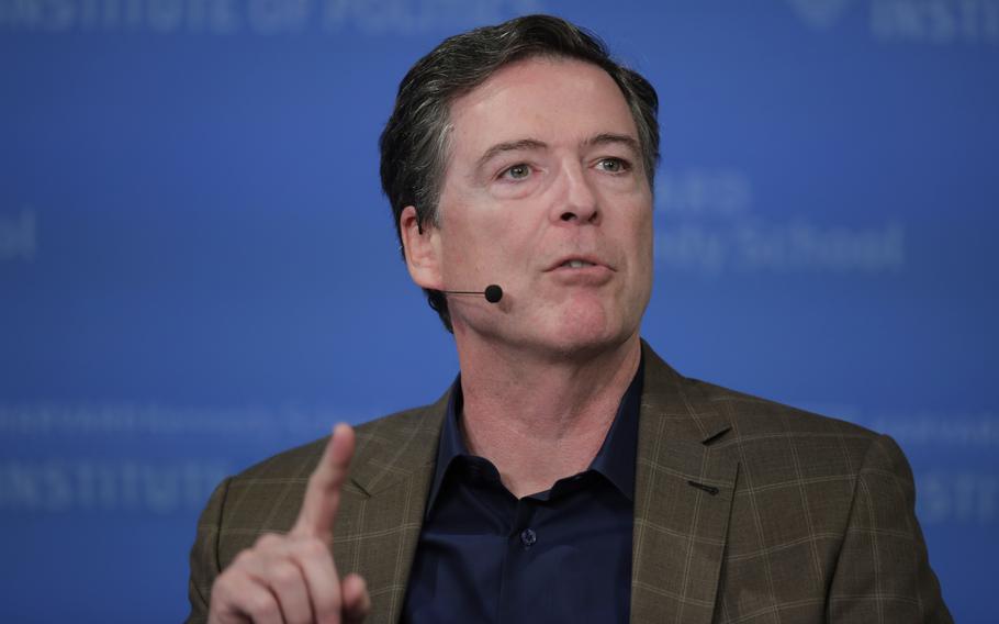 A man in a brown blazer speaks into a headset microphone while gesturing with his right hand.