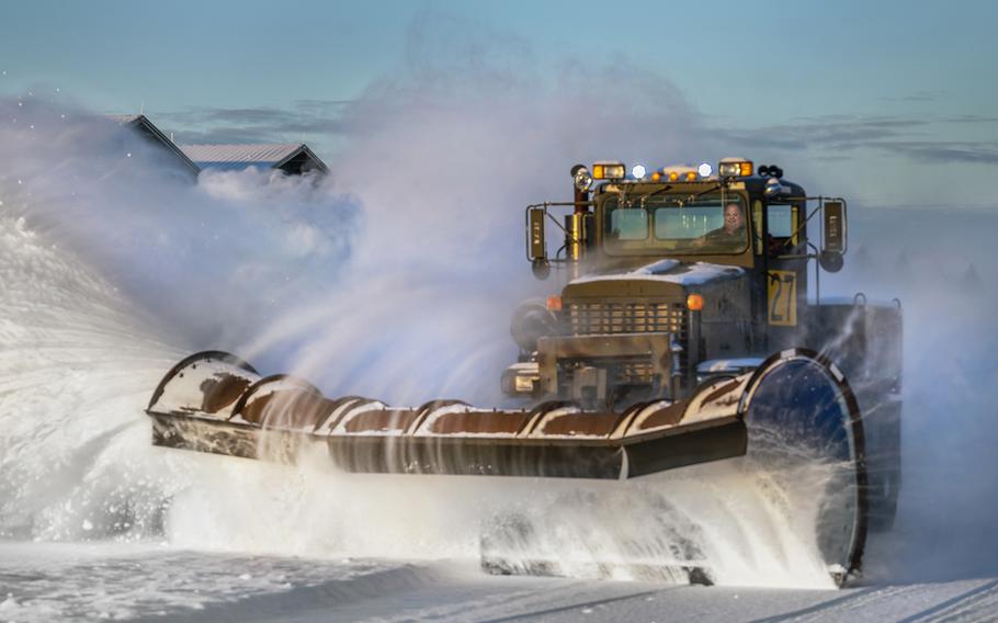 An airman clears snow with a snowplow.