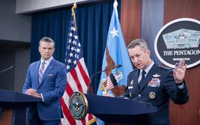 Gen. Dan Caine on the right, raising his hands in gesture at a podium, while Defense Secretary Pete Hegseth looks on from another podium on the left.