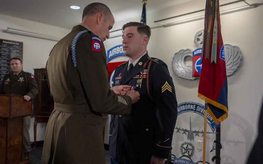 Commander places medal on soldier’s uniform as he stands at attention.
