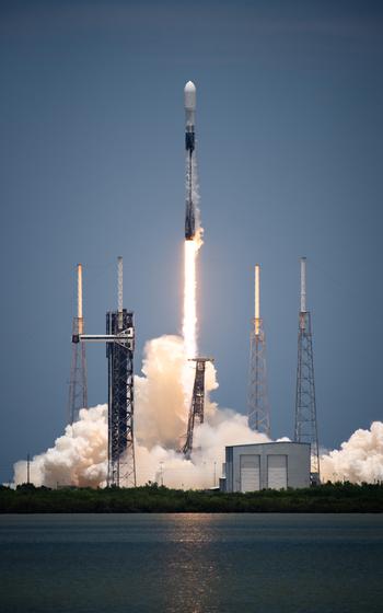 A vertical photo of a rocket lifting off from a launch pad.