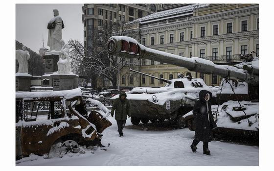 People walk past destroyed Russian military vehicles covered in snow in front of St. Michael's Golden-Domed Monastery in downtown Kyiv on Dec. 8, 2023.