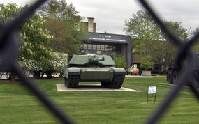 A view of a tank and the base sign on a building through the fence.